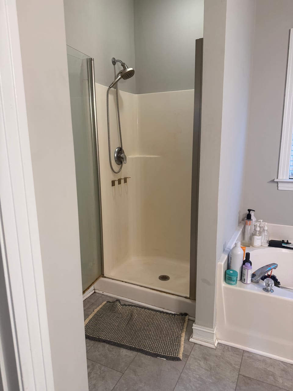 The old fiberglass shower stall with a framed frosted door, next to a garden tub