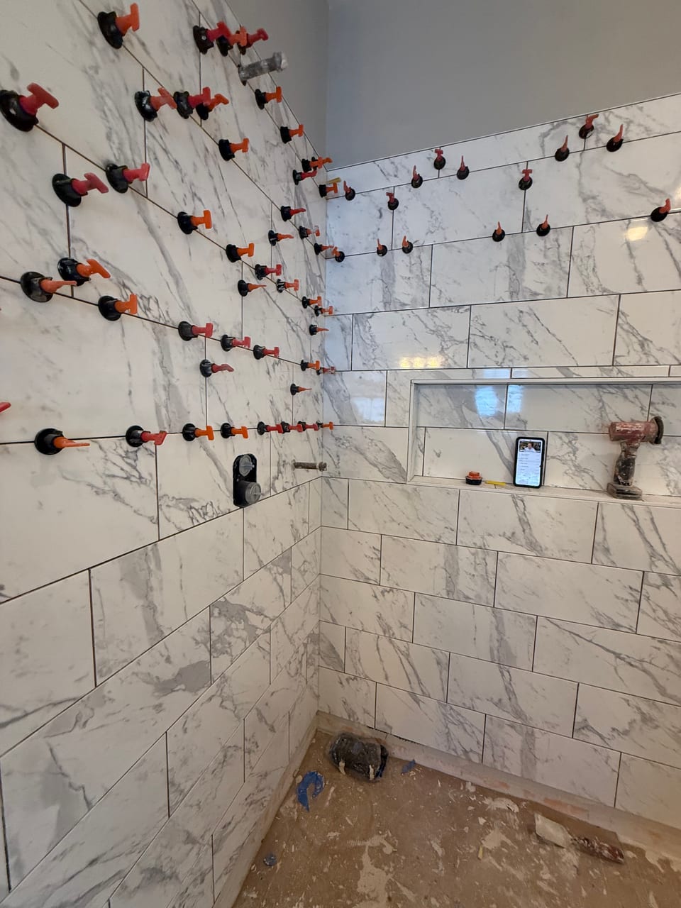 Marble-look wall tile going up with leveling clips still in place
