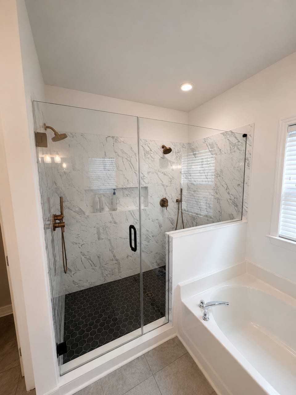 The finished shower with marble-look tile, a black hex mosaic floor and frameless glass