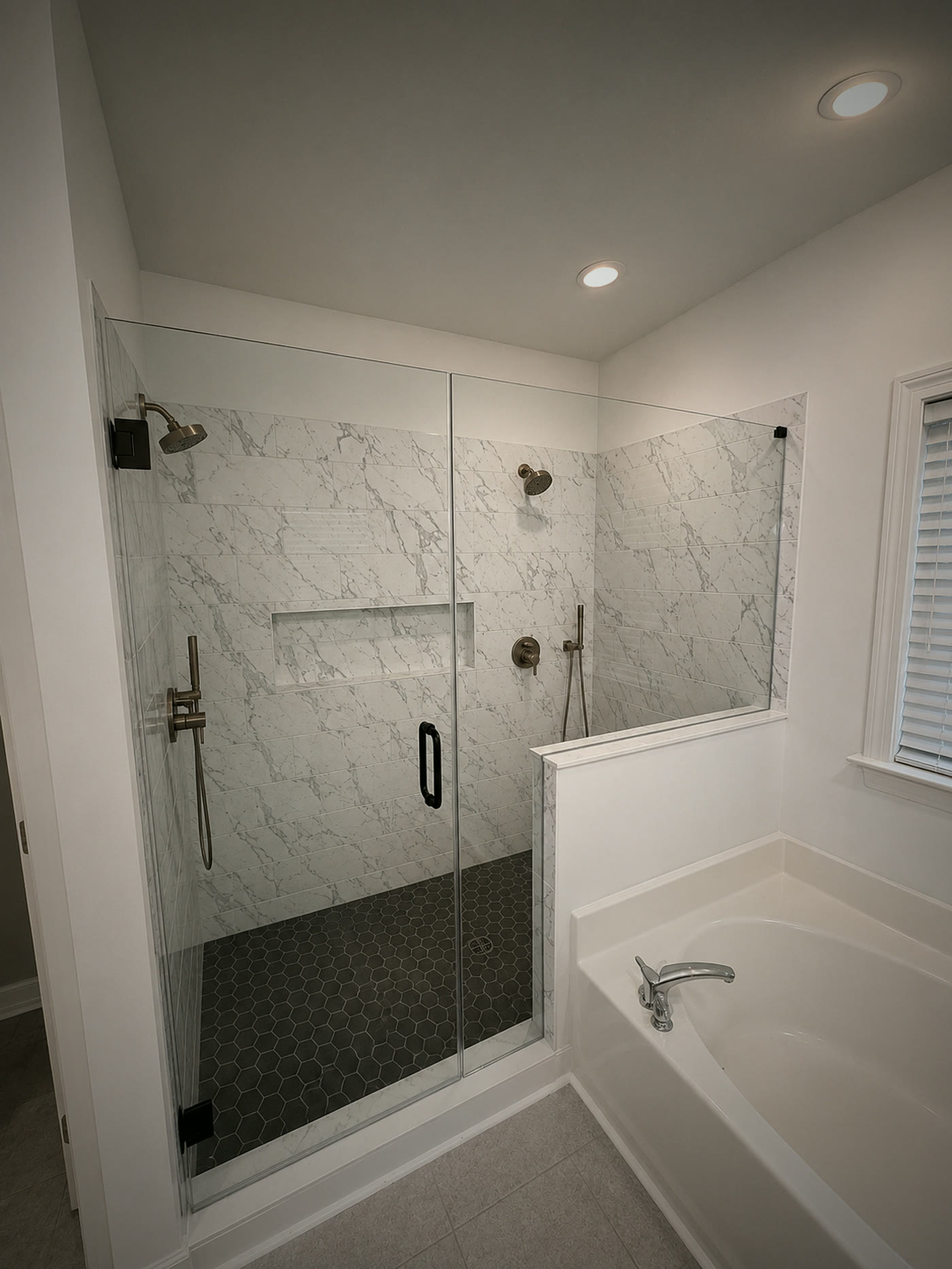 A finished master bathroom in Cornelius, NC with marble-look tile to the ceiling, a black hex mosaic shower floor and frameless glass