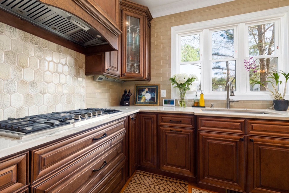 A dated kitchen with dark wood cabinets, a heavy wood range hood and a busy tile backsplash