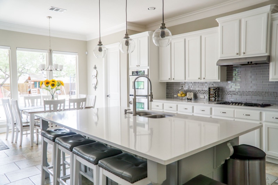 The finished kitchen with white shaker cabinets, a large quartz island, pendant lights and stools